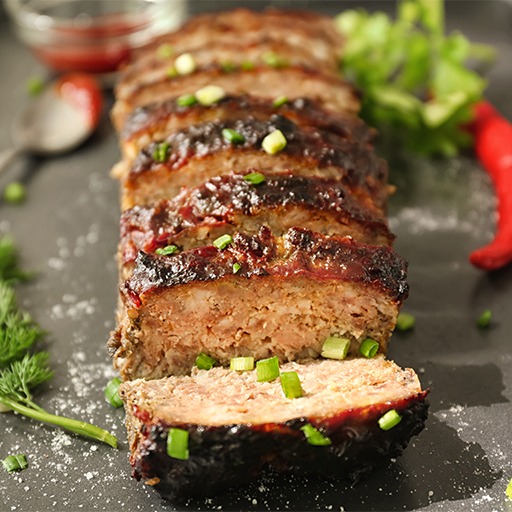 A succulent meatloaf topped with sauce and herbs, elegantly presented on a sleek black tray.