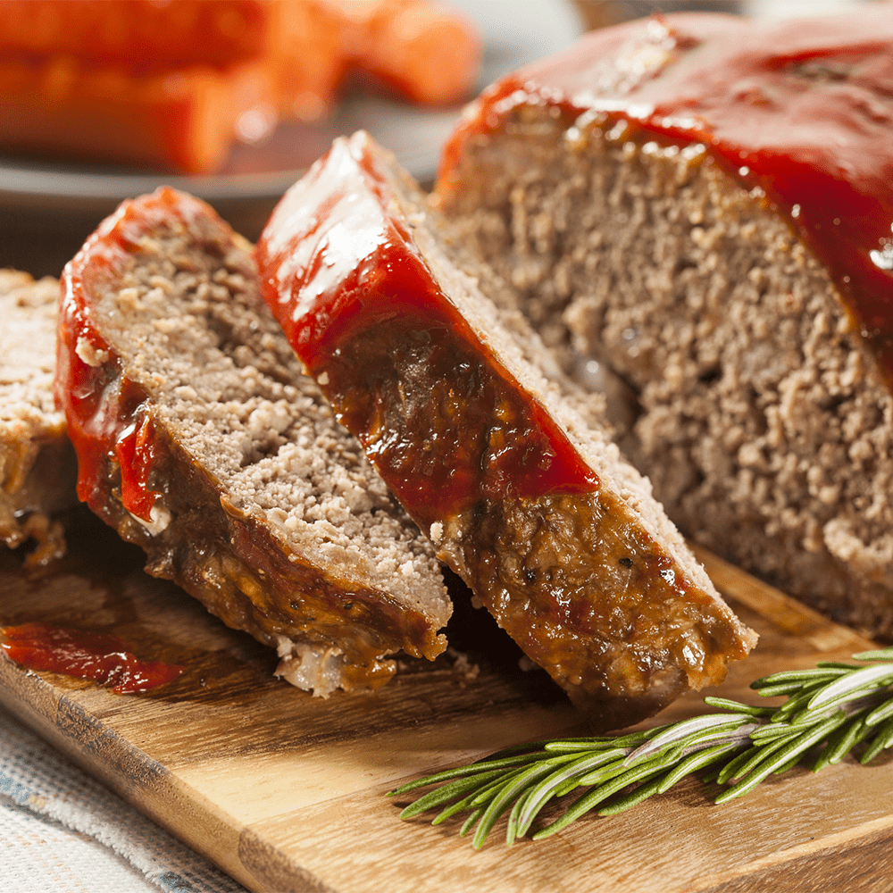 A meatloaf topped with ketchup and garnished with rosemary, displayed on a wooden cutting board.