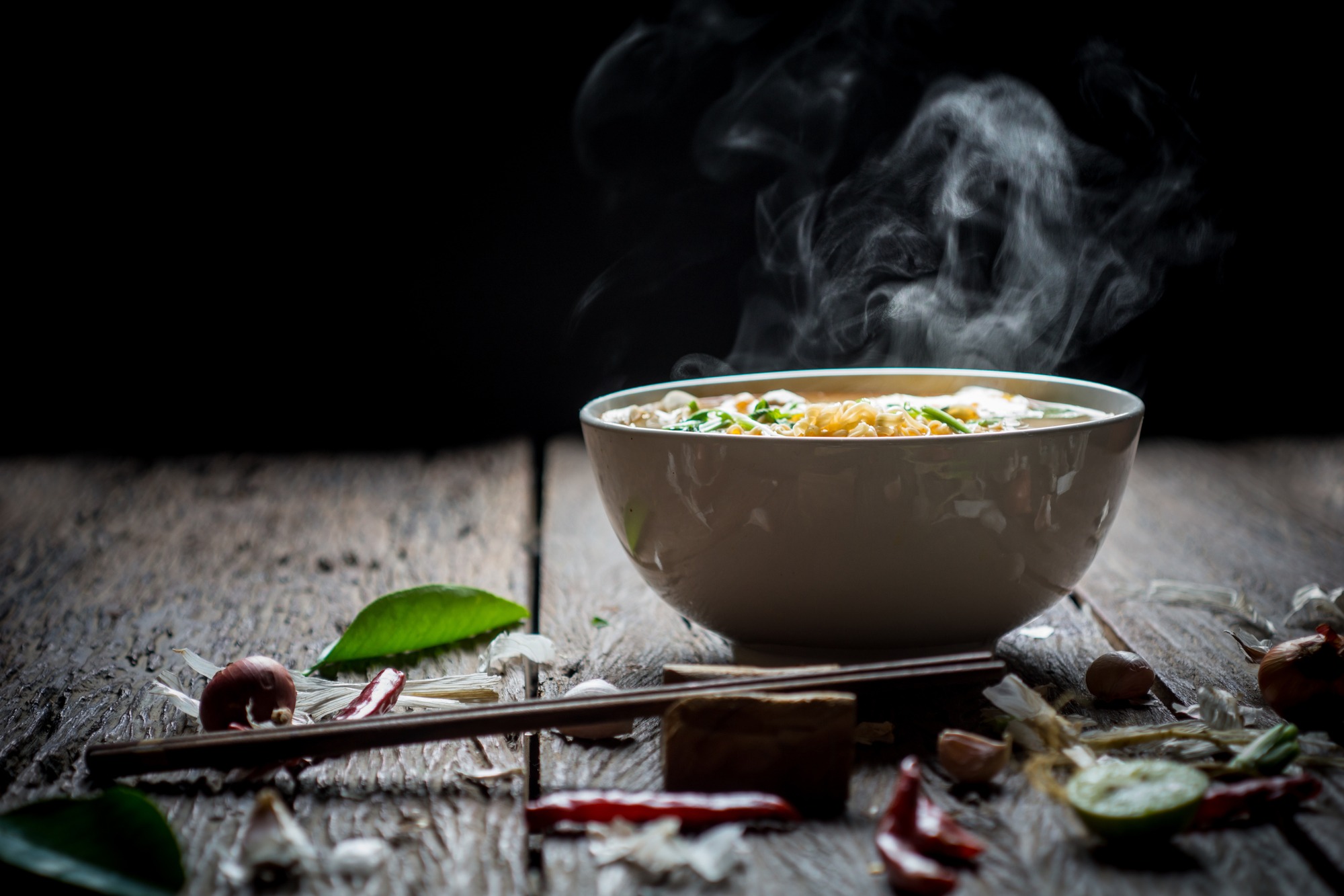 Noodles with steam and smoke in bowl on wooden background, selective focus. Asian meal on a table, junk food concept