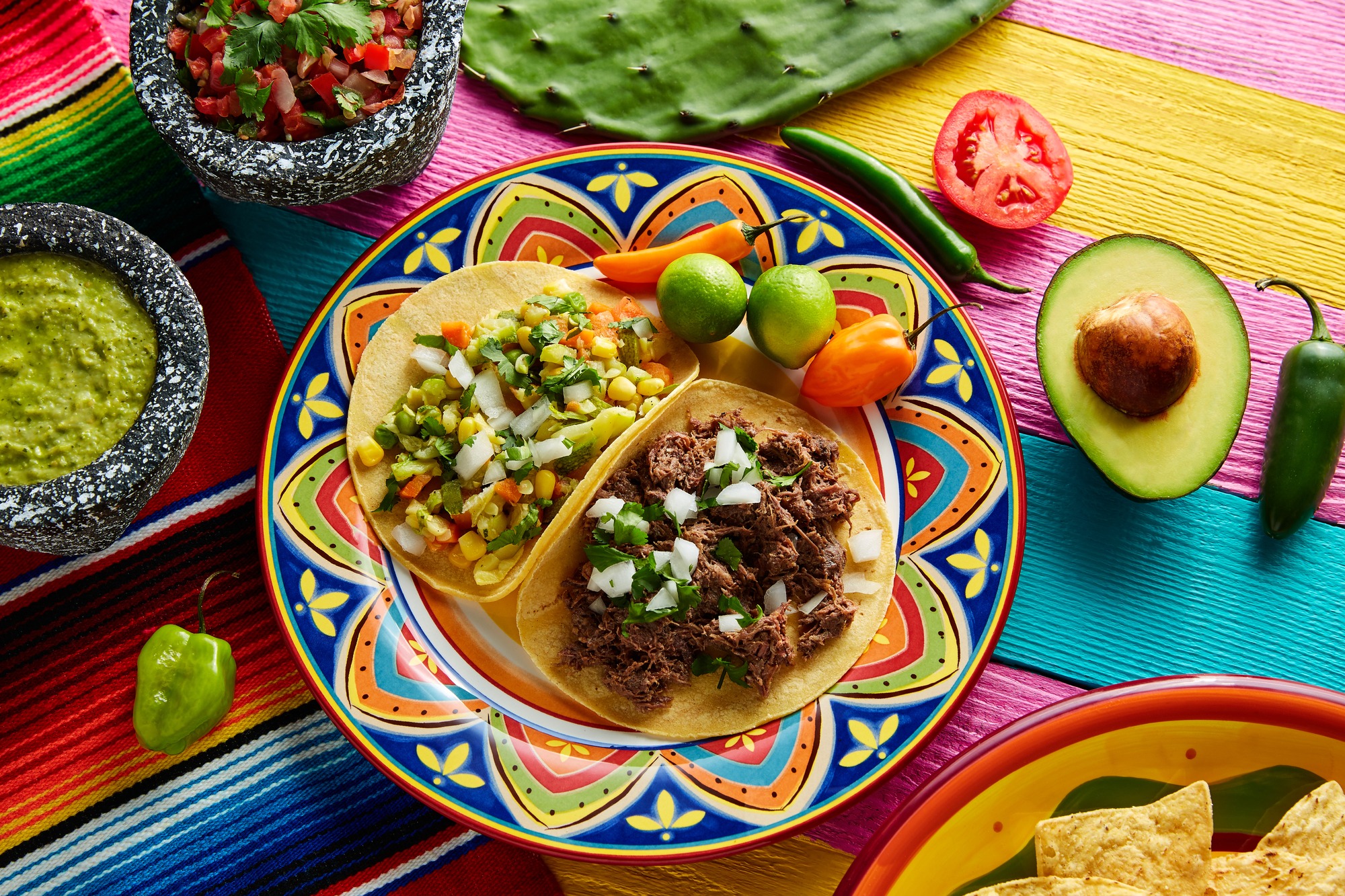 Mexican platillo tacos of barbacoa and vegetarian with sauces and colorful table